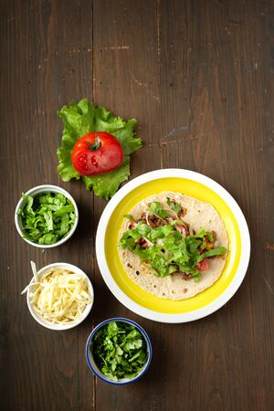 Yellow plate mexican beef tacos with condiment tomato, lettuce, coriander, cheese on a wooden tableの写真素材