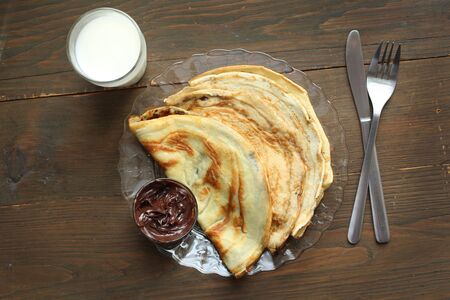 Top view of three pancakes fill with hazelnuts chocolate and a glass of milk on a wooden backgroundの写真素材