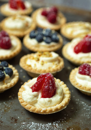 Strawberry tartlet with blueberry, raspberry and pistachios tartlets on a metal plate and powder sugarの写真素材