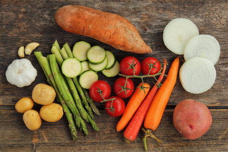 Different vegetable display on a wooden table. Sweet potato, garlic, yellow potato, tomato, carrot, red potato, onion, asparagus and zucchiniの写真素材