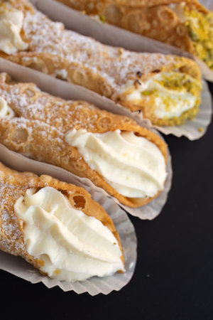 Fresh plain cannoli and with pistachios in paper on a black backgroundの写真素材