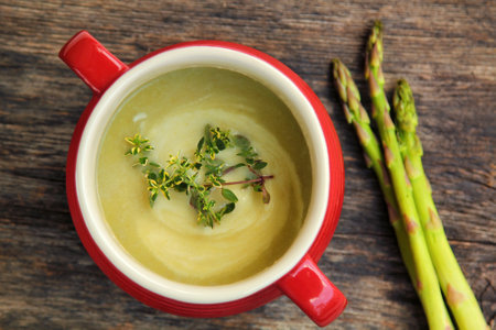 Asparagus soup in a red bowl with fresh vegetables on the side on a wooden backgroundの写真素材