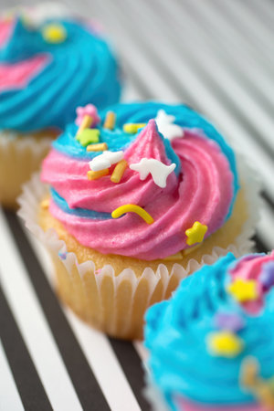 Cupcakes in a row with blue and pink icing on a black and white lined backgroundの写真素材