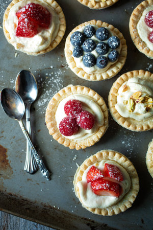 Top view of blueberry, strawberry and pistachios tartlets with custard on a wooden tableの写真素材
