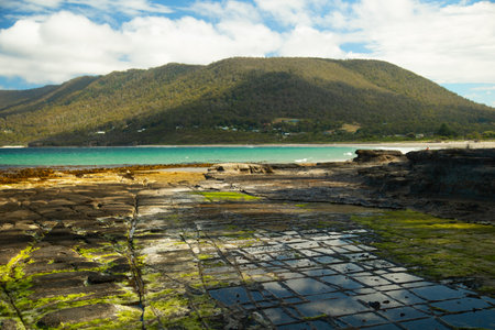 Tessellated pavement in Tasmania is a stunning place formed by patterned stilstone with the tasman sea in the background and a mountain.の写真素材