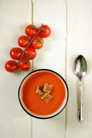 Tomato soup with spoon on a white background and fresh cherry tomatoesの写真素材