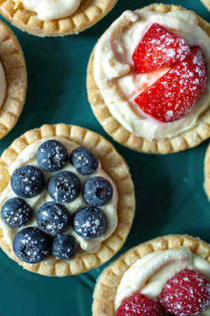 Top view of blueberry, strawberry and pistachios tartlets with custard on a green backgroundの写真素材