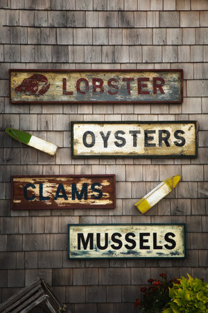 Old signs on a wooden shingle wall. Seafood notices for lobster, mussel, oyster and clam.の写真素材