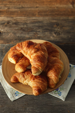Fresh homemade croissant in a bamboo plate on a rustic wooden backgroundの写真素材