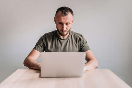 Being concentrated. Young handsome bearded man working remotely from home on laptop.の写真素材