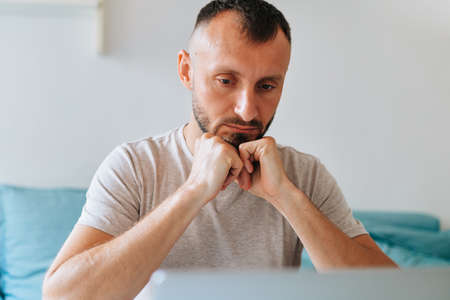 Being focused. Overthinking. Young handsome man working on laptop from home. Human and technology concept.の写真素材