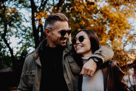 Autumn walk. Couple. Love. Man and woman in warm casual clothes are hugging and smiling while walking down in the parkの写真素材