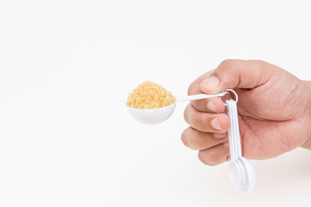 hand picking up brown sugar with measuring spoonの写真素材