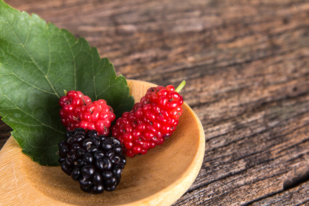 mulberry fruit in the wooden spoon on a wood plateの写真素材