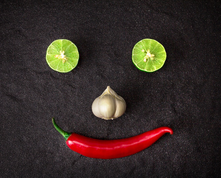red chili , garlic and lime lemon arrange as the smiling face on black stone backgroundの写真素材