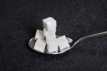 cloose up the white sugar cubes in metal spoon on black stone plate backgroundの写真素材