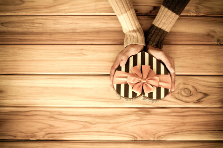 Hand holding heart gift box shape on wooden backgroundの写真素材