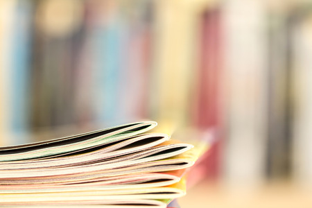 Close up edge of colorful magazine stacking with  blurry bookshelf background for publication and publishing concept , extremely shallow DOFの写真素材