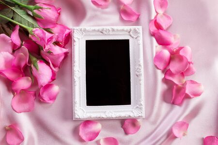Empty photo frame with a bouquet sweet pink roses  petal on  soft pink silk fabric , romance and love card conceptの写真素材