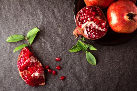 Fresh red pomegranate and seed  with leaves over black stone background , overhead or top viewの写真素材