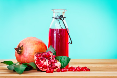 fresh red pomegranate juice with pomegranate seed and fruit with leaf on wooden table and blue background , healthy drink . の写真素材