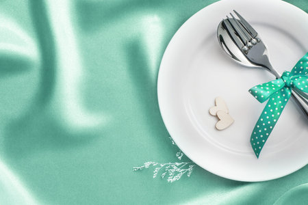 wooden heart shape with White empty plate with fork and spoon on pastel green silk fabric for love dinner conceptの写真素材