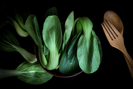 close up Fresh baby green bok choy in bowl with wodden spoon and fork on black background , overhead or top view shotの写真素材