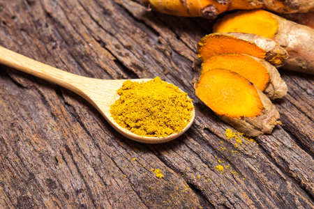 the turmeric powder in spoon and roots on wooden plate