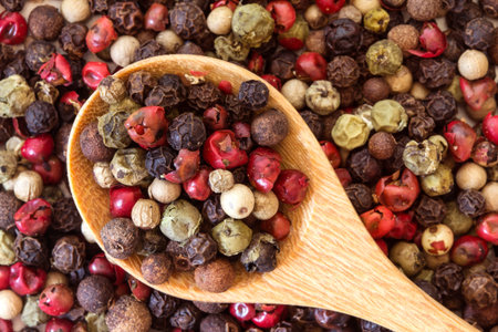 Close up mixed type of the peppercorns in wooden spoon on the peppercorns background