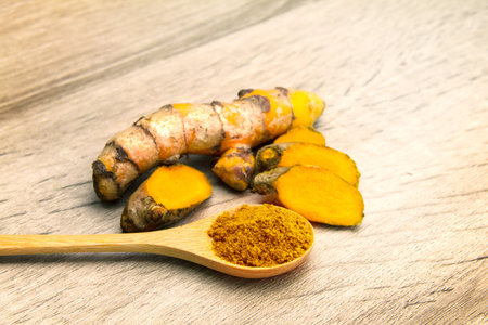 the turmeric powder in spoon and roots on wooden plate