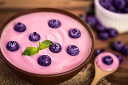 close up pink creamy homemade blueberries fruit yogurt with fresh green mint leaf on wooden table backgroundの写真素材