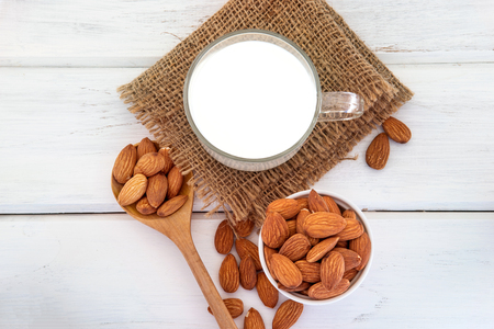 Close up top view of healthy almond milk in drinking glass with seed in white cup and wooden spoon on white wooden table plate with copy spaceの写真素材