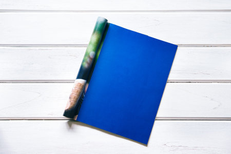 Opened empty dark blue mock up magazine page on white wooden table background