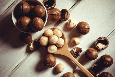 Close up Macadamia nuts on  white wooden background , superfood and healthy food concept , overhead or top view shot with vintage color toneの写真素材