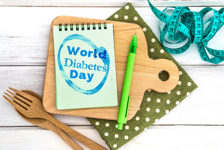 Notepad with World Diabetes Day text on the chopping board with wooden fork and spoon and the measuring tape on white table , Diabetes world day on 14 November encourage awareness campaign background conceptの写真素材