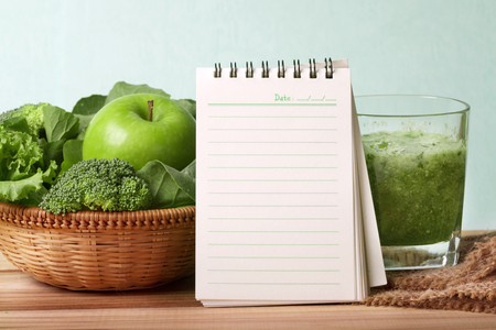 blank note pad and the Healthy fresh  green smoothie juice in  glass bottle on wooden table with green apple and  vegetables basket for healthy detox and diet  habits concept の写真素材
