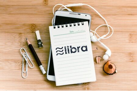 Libra coin cryptocurrency and blockchain symbol on notepad with  pencil and smart phone on wooden table, New digital currency conceptの写真素材
