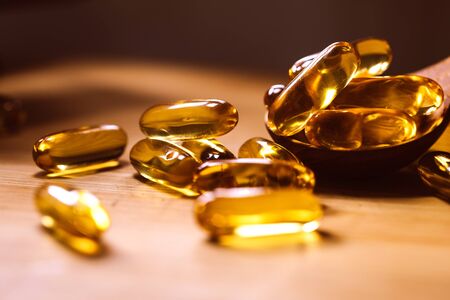 Close up vitamin D and Omega 3 fish oil capsules supplement on wooden plate for good brain, heart and health eating benefitの写真素材