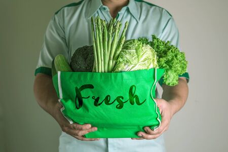 close up hand holding green grocery bag of mixed organic green vegetables, healthy organic green food shopping and diet healthcare nutrition therapy conceptの写真素材