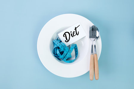 measuring tape with dish and spoon decoration on a blue background , diet tag for dieting conceptの写真素材