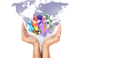Hand holding covered multi colorful cancer awareness ribbon with world map design for campaign of World Cancer Day banner and backgroundの写真素材