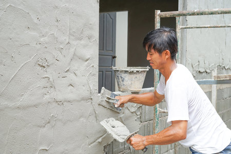 an middle age asian man looks happy, sweating while plastering cement wall at home like a hobby, selective focusの写真素材