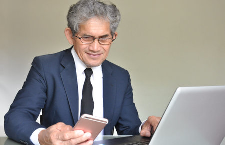 senior man wear suit typing laptop and looking mobile phone while working in the office, selective...