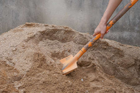 pile of sand, hand of a construction worker scooping sand for mix mortar on construction site, selective focus.の写真素材