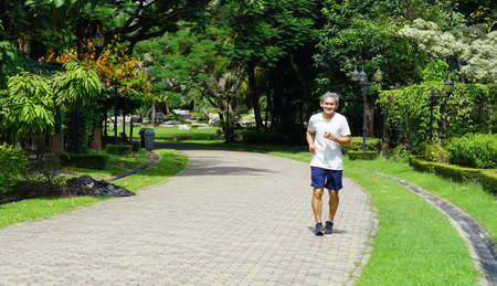 an old man is jogging among the nature atmosphere (selective focus), concept heath care, lifestyle, activity in elderly peopleの写真素材