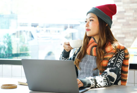 Portrait asian  woman work with laptop on table, sitting near glass window, relaxing by sip a drink...