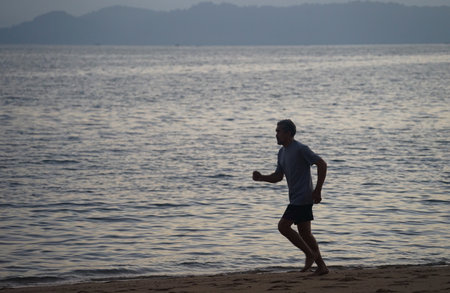 silhouette running movement of senior man with barefoot on the beachの写真素材