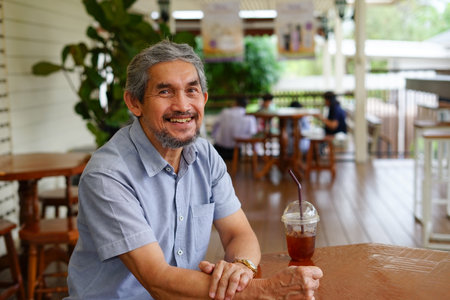 smiling senior man sitting casually in cafe outdoor and a cup of iced coffee on tableの写真素材