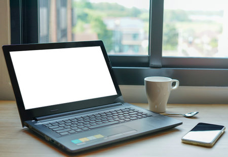 Laptop with white screen, mobile phone and coffee cup on desk.concept technology business work equipmentの写真素材
