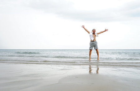 A happy senior man jumping on the beach in the sea water